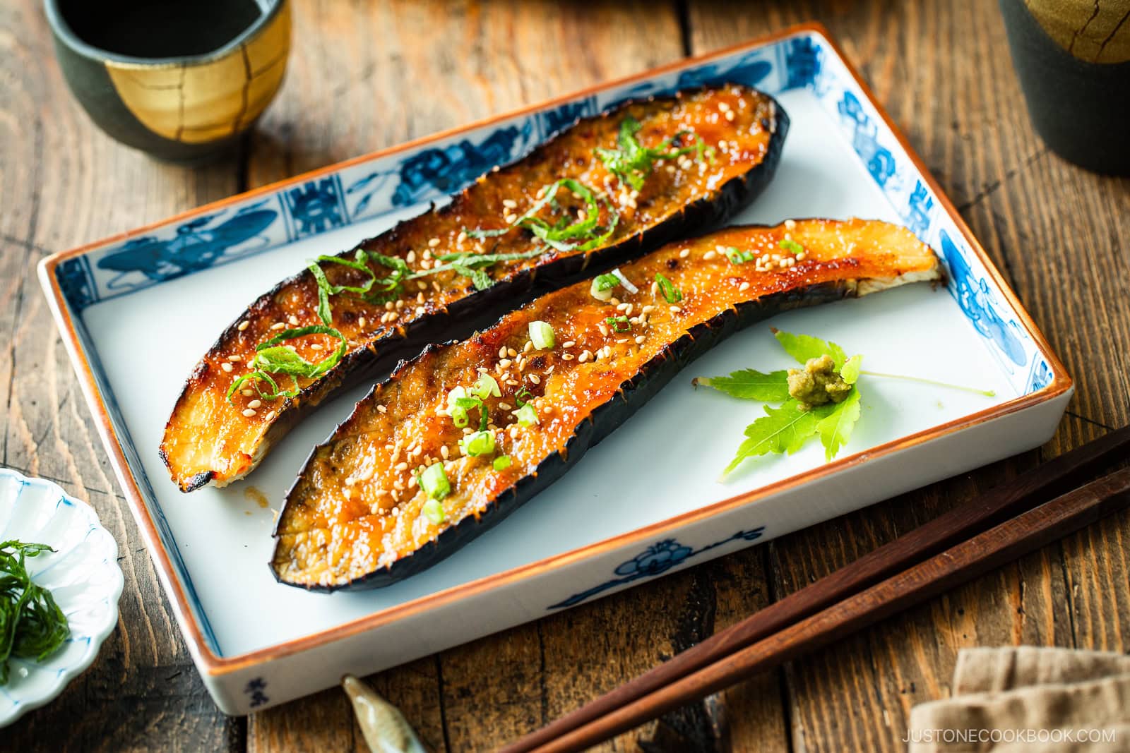 A rectangular plate containing Miso Glazed Eggplant garnished with yuzu kosho paste on a green maple leaf on the side.
