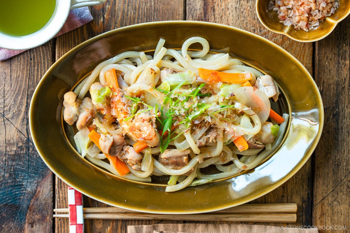 An olive colored oval plate containing Yaki Udon, Japanese stir-fried udon noodles with chicken and vegetables.