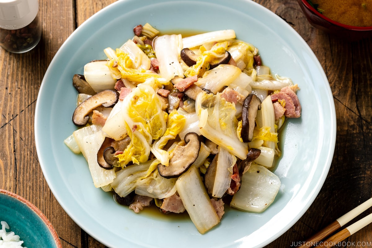 A round ceramic plate containing napa cabbage stir-fry with shiitake mushrooms and bacon seasoned lightly with soy sauce.