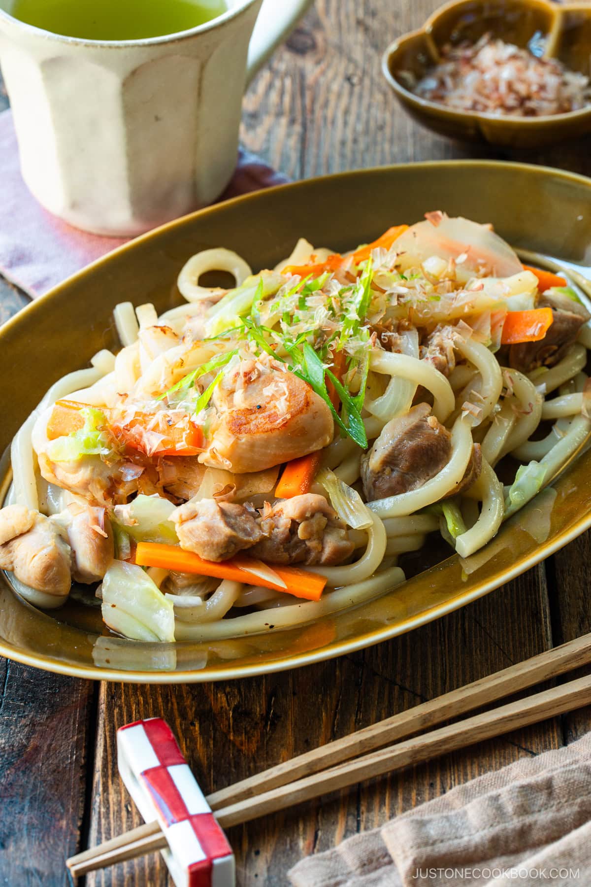 An olive colored oval plate containing Yaki Udon, Japanese stir-fried udon noodles with chicken and vegetables.