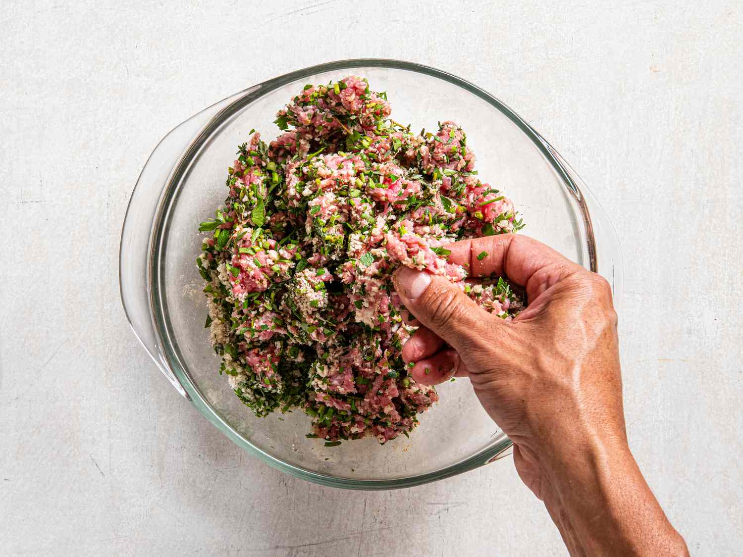 pork and herbs mixed together by hand in a bowl 