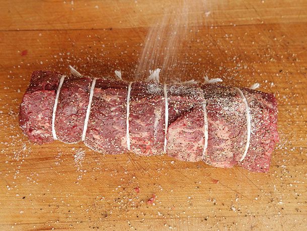 Seasoning a tied beef tenderloin with salt and pepper for beef Wellington.