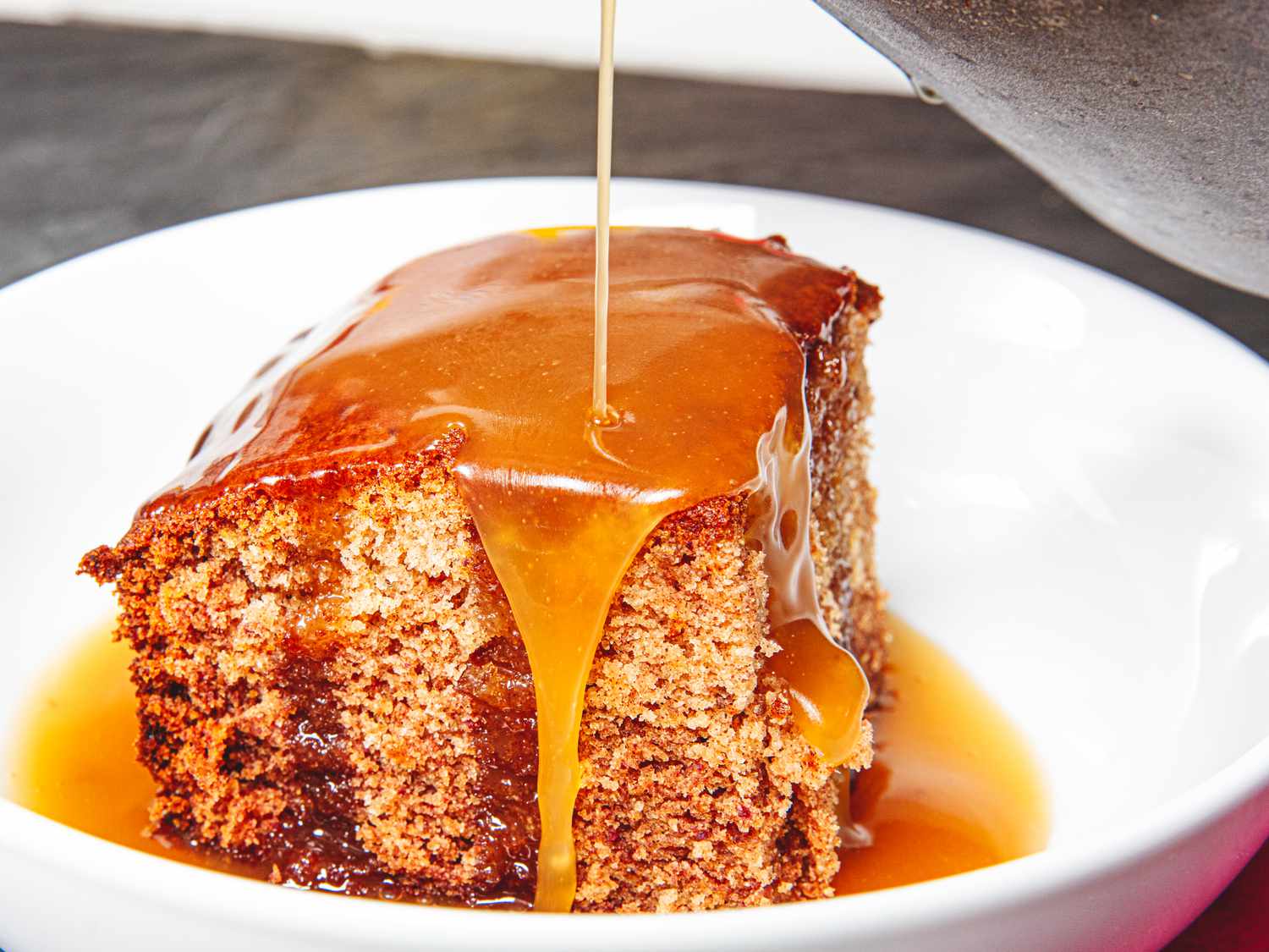 Side view of pouring sauce on sticky toffee pudding 