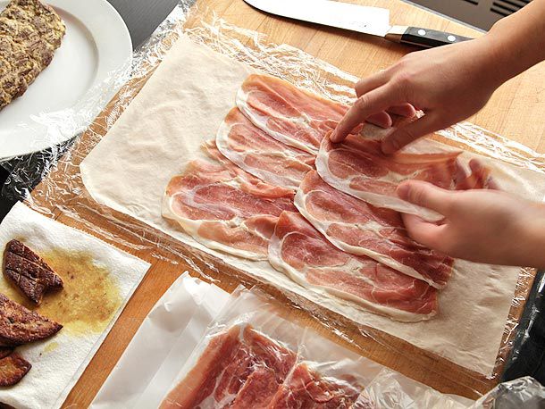 Laying sheets of prosciutto on top of phyllo dough on plastic wrap before adding foie gras and beef tenderloin for beef Wellington.