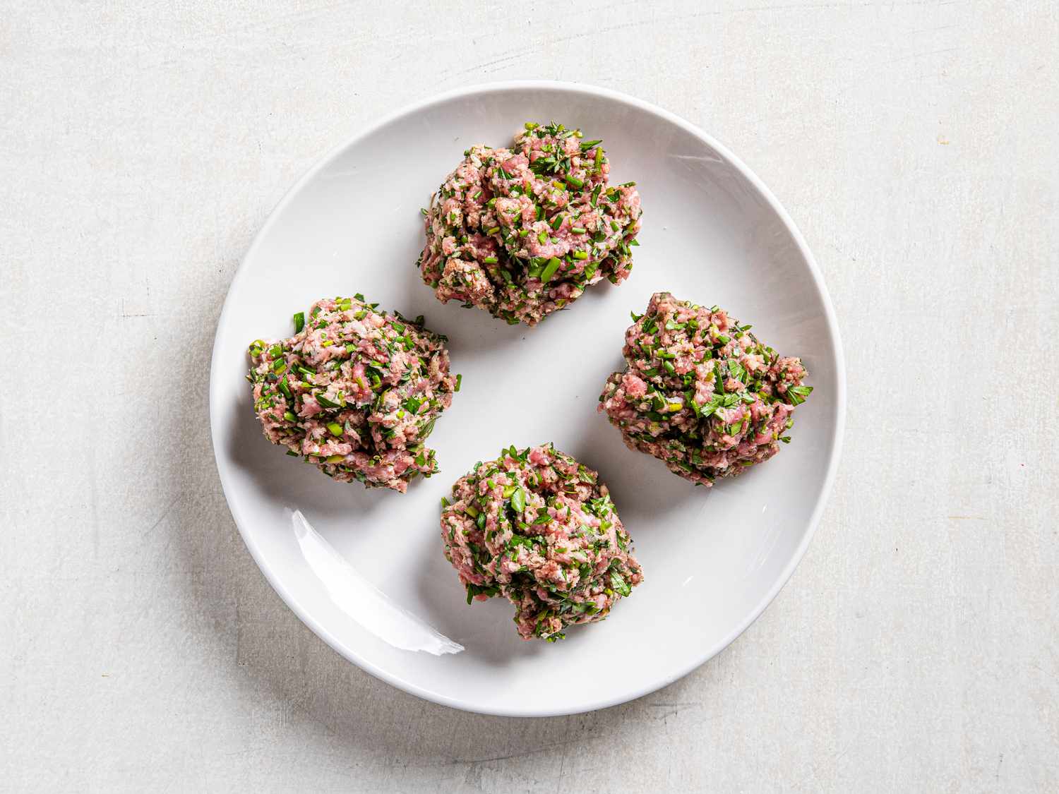 meat and heb mixture split into 4s, on a white plate 