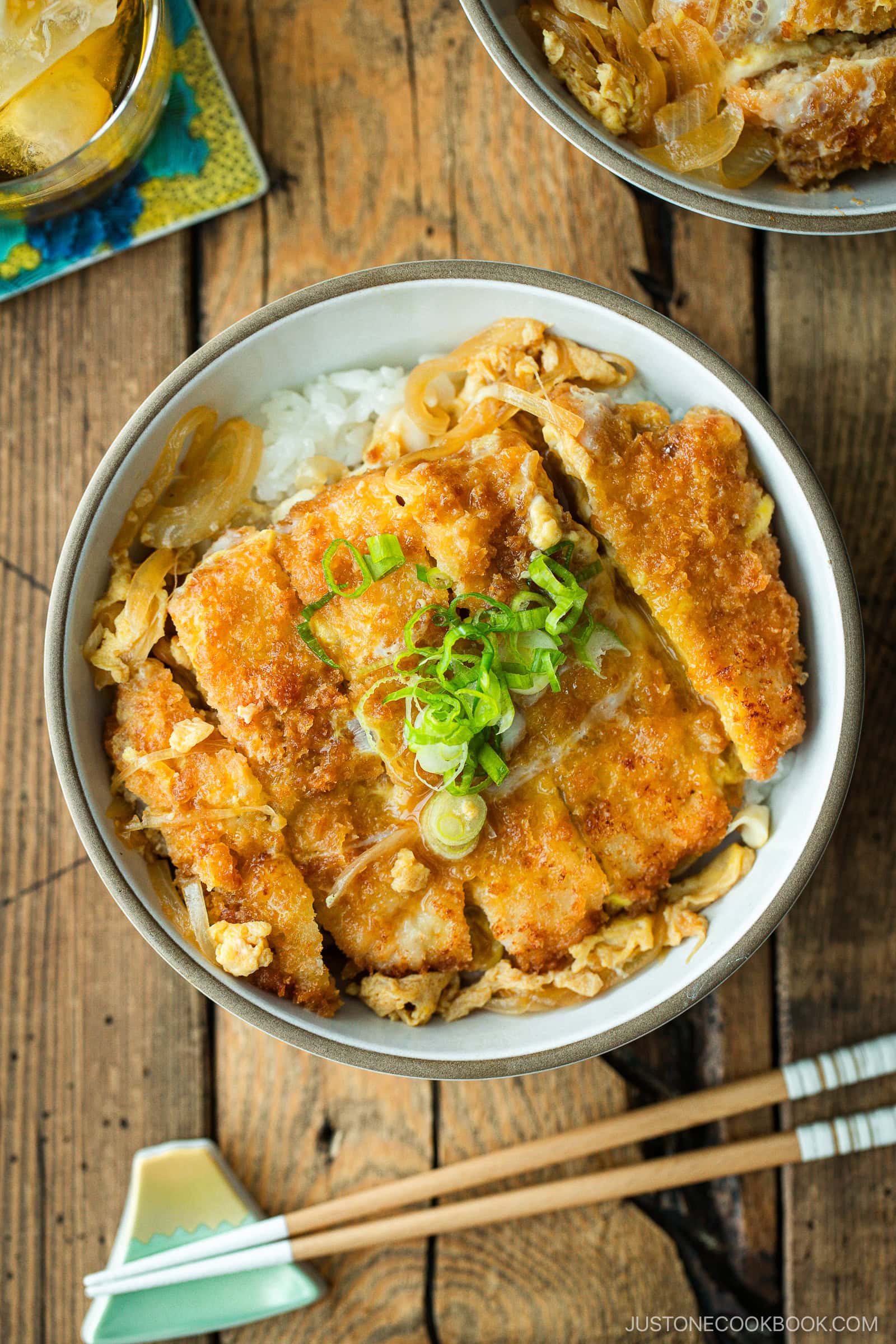 A white bowl containing Katsudon, pork cutlet rice bowl, where golden brown tonkatsu, drizzled egg, and tender onion are simmered in a savory dashi broth.