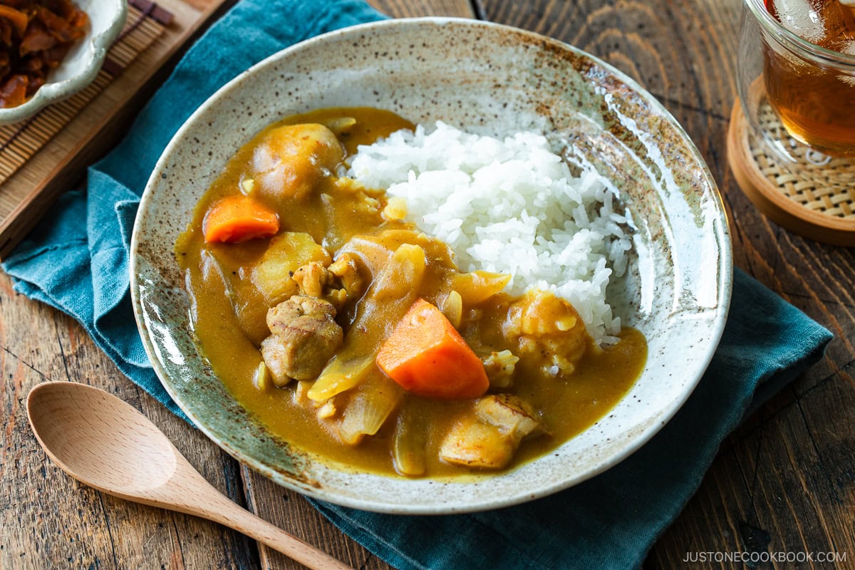 A round plate containing Japanese chicken curry over steamed rice, garnished with fukujinzuke pickles.