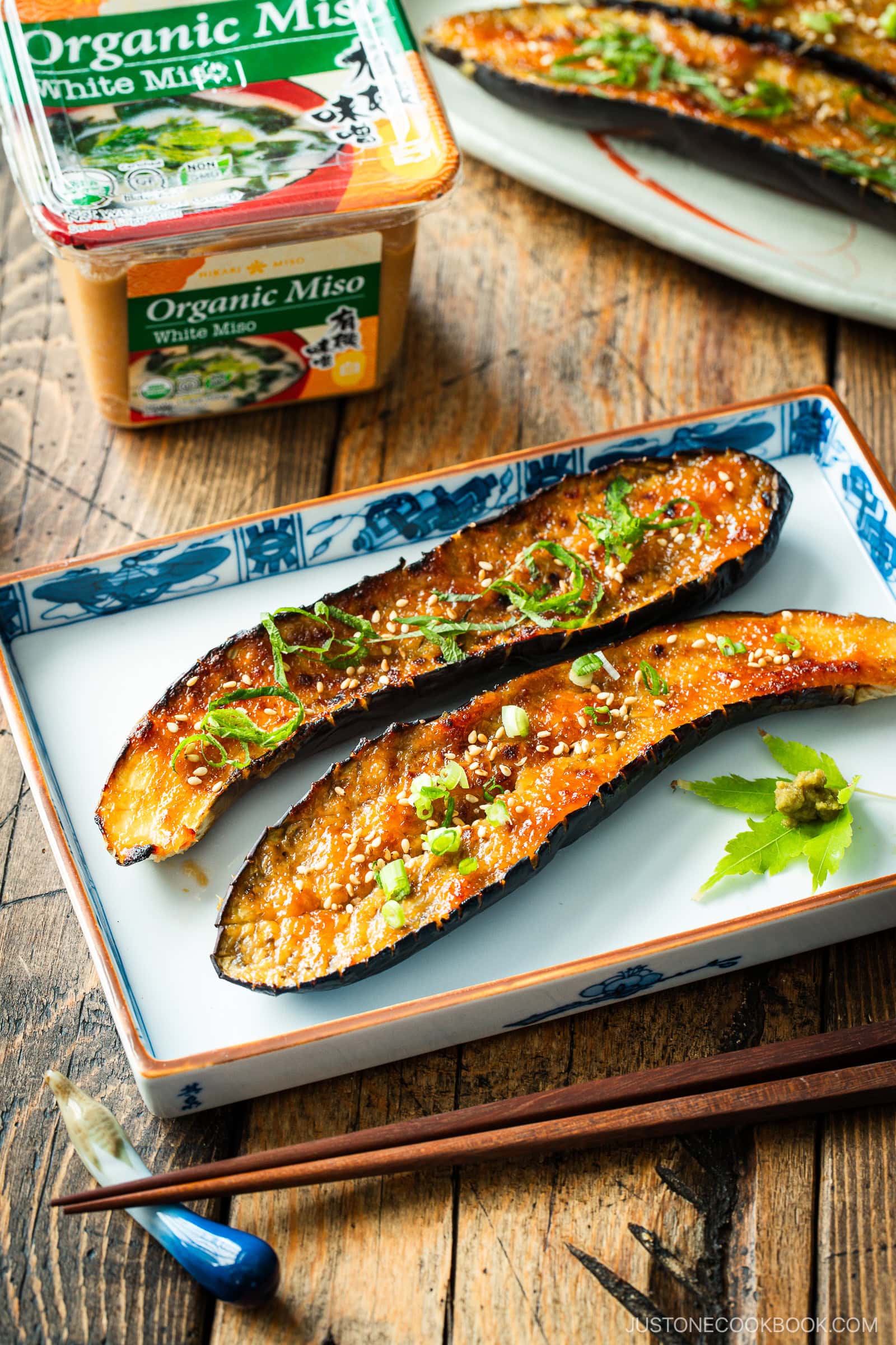 A rectangular plate containing Miso Glazed Eggplant garnished with yuzu kosho paste on a green maple leaf on the side.