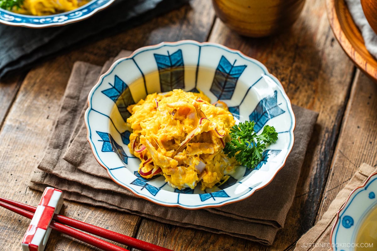 A Japanese round plate containing velvety and rich Kabocha Salad with crisp and refreshing red onion slices and ham, mixed with cream cheese and tangy Japanese mayo.