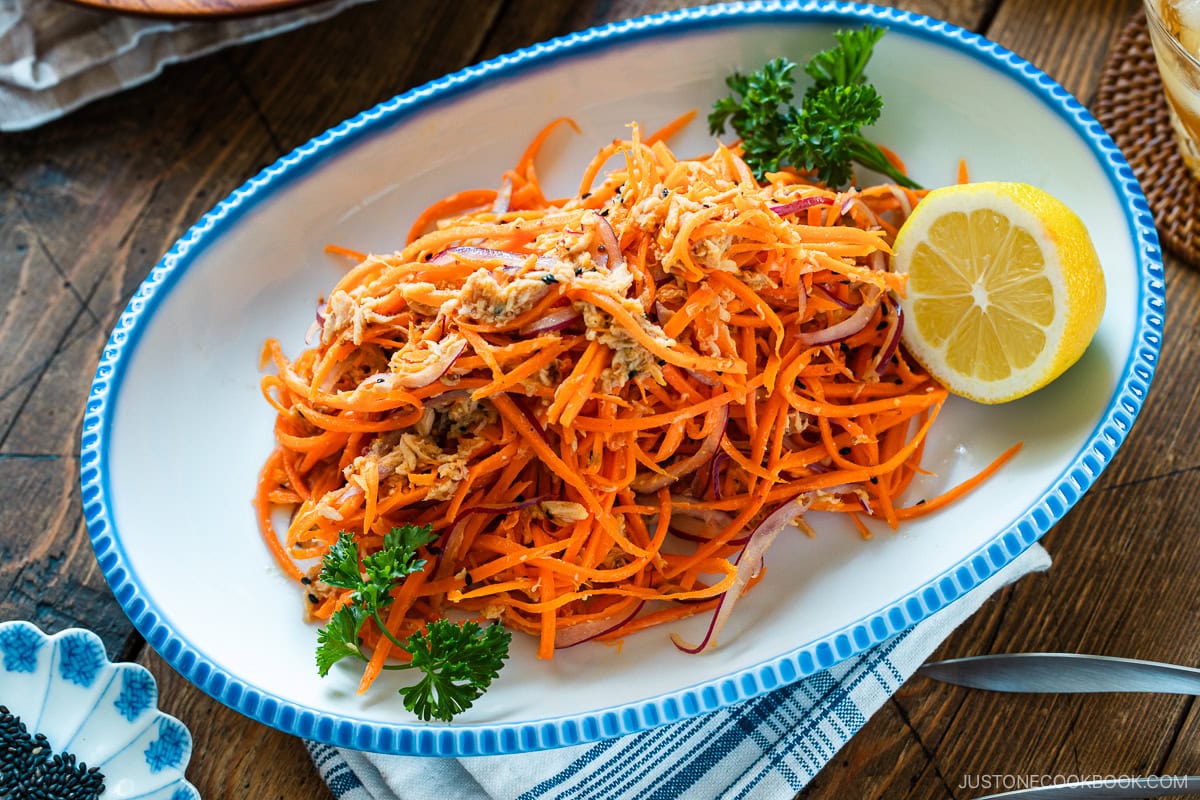 An oval scalloped plate containing shredded carrot and tuna salad garnished with parsley and lemon.