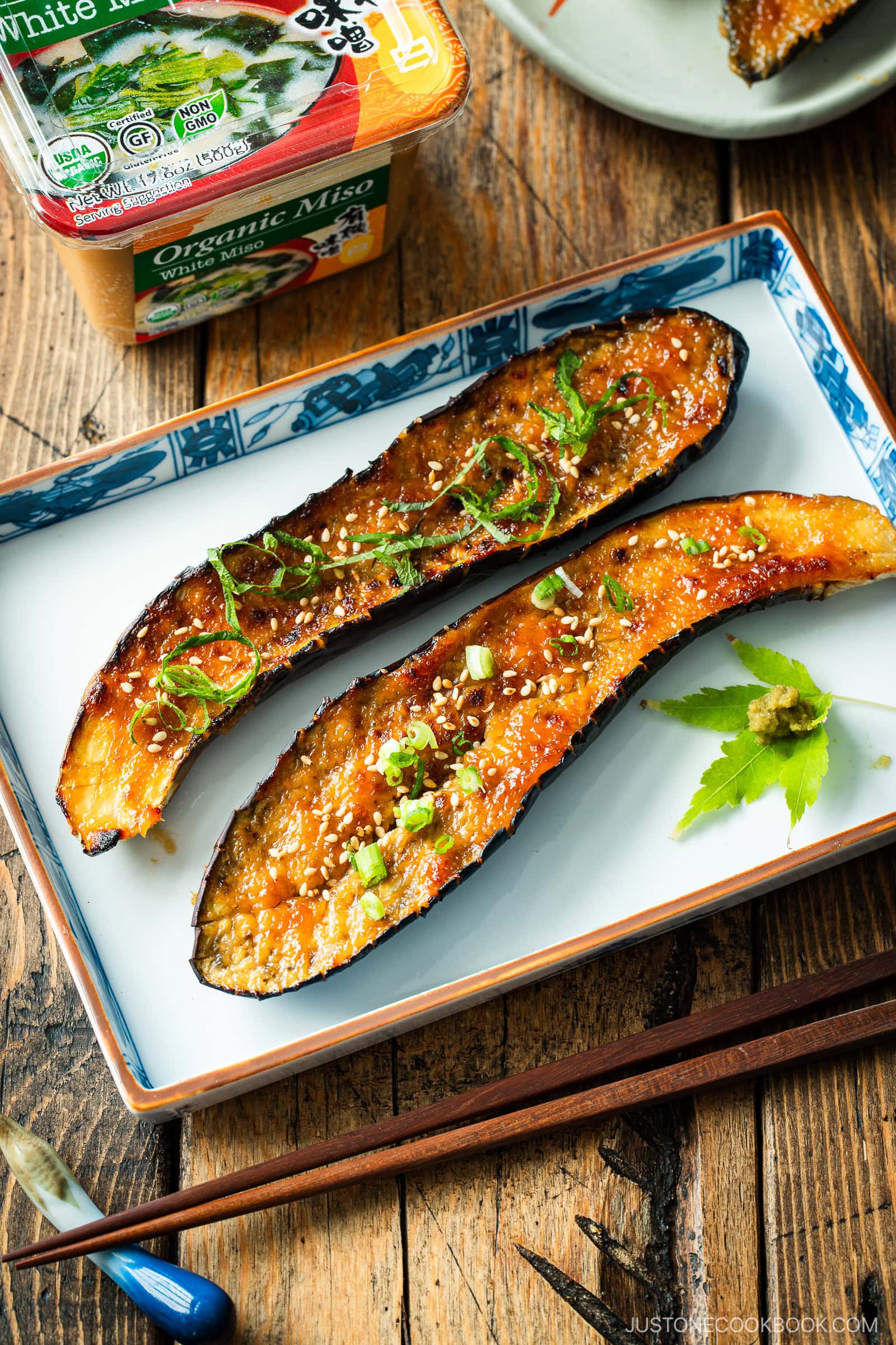 A rectangular plate containing Miso Glazed Eggplant garnished with yuzu kosho paste on a green maple leaf on the side.