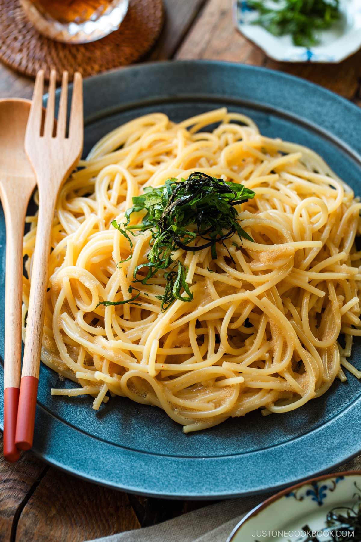 A black round plate containing metaiko pasta - Japanese spaghetti with spicy salted cod roe topped with julienned shiso and shredded nori seaweed.