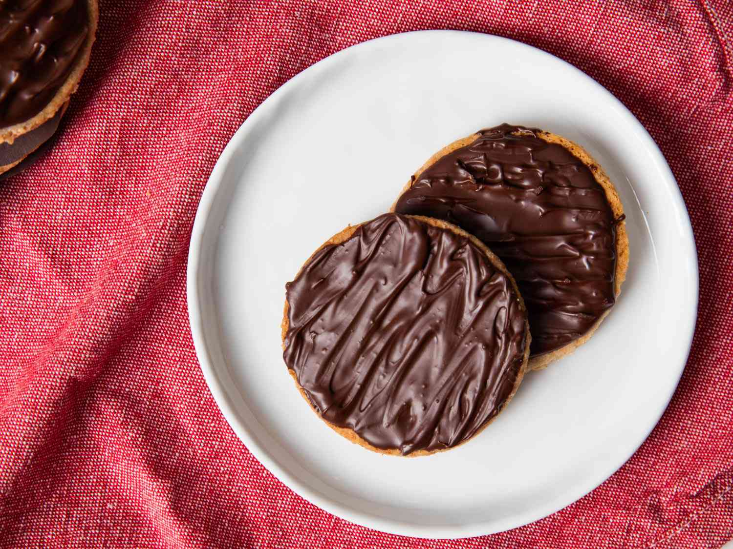 An overhead shot of two digestive biscuits sitting on a white plate.