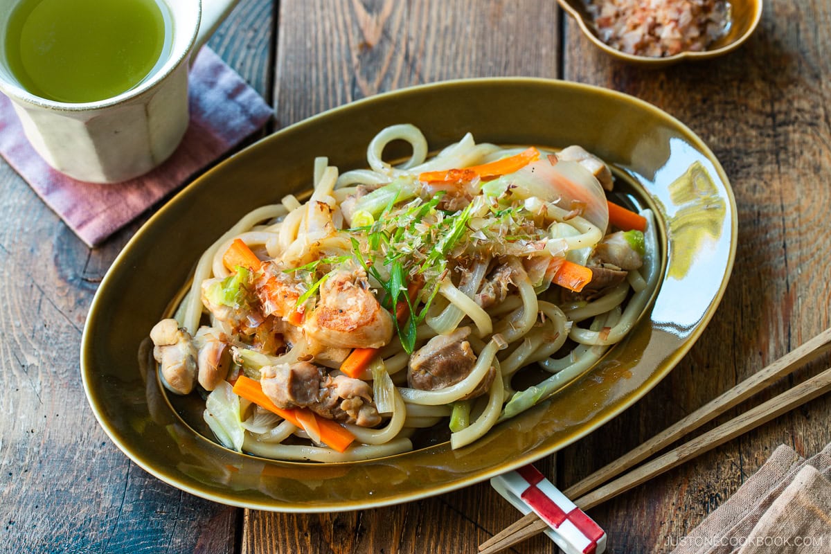 An olive colored oval plate containing Yaki Udon, Japanese stir-fried udon noodles with chicken and vegetables.