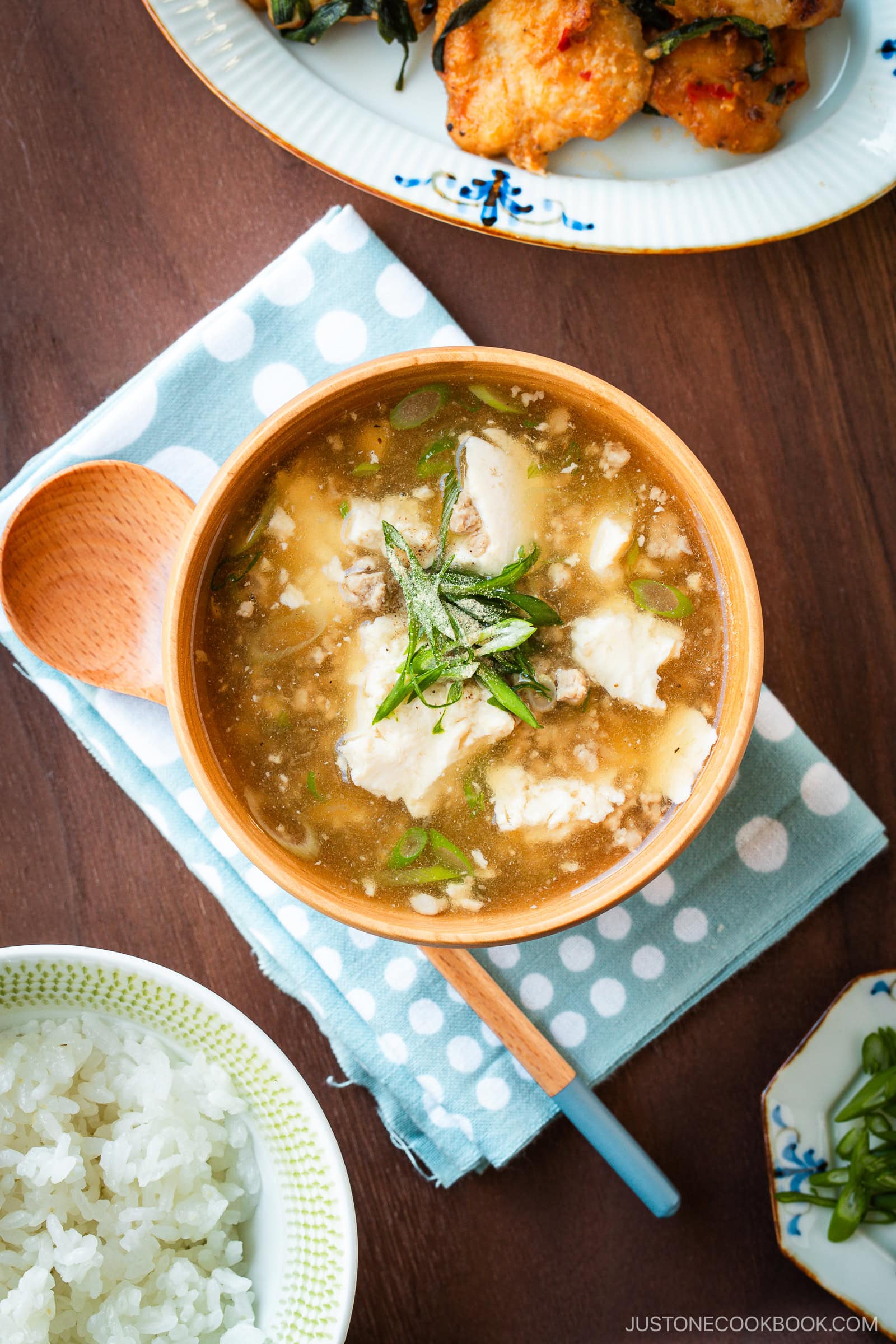 Wooden bowls filled with Pork Tofu Soup, served alongside steamed rice and a chicken dish on the table.