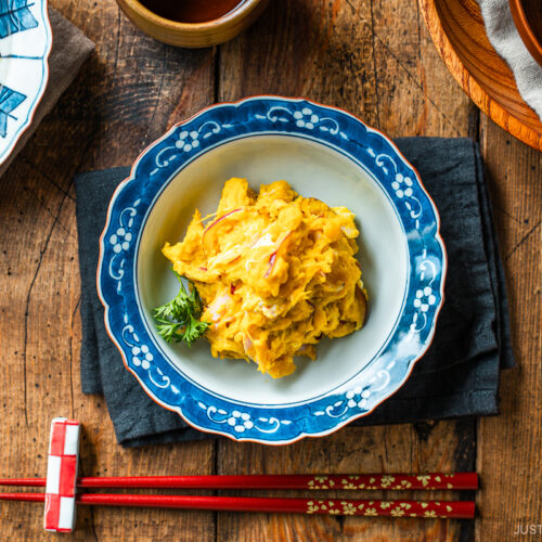 A Japanese round plate containing velvety and rich Kabocha Salad with crisp and refreshing red onion slices and ham, mixed with cream cheese and tangy Japanese mayo.