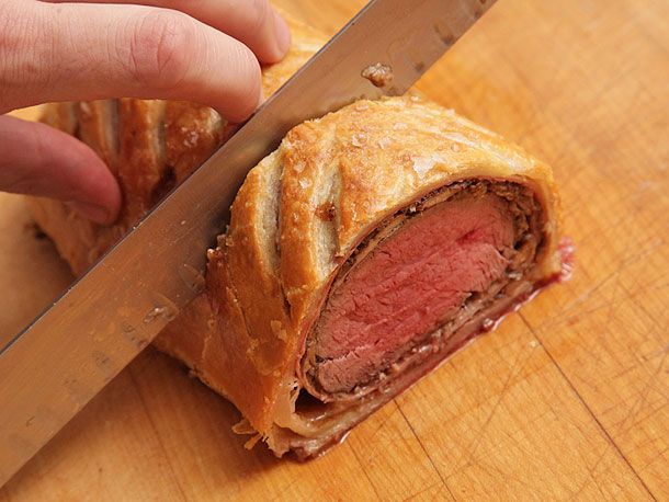 Slicing perfectly cooked beef Wellington on a wooden cutting board.