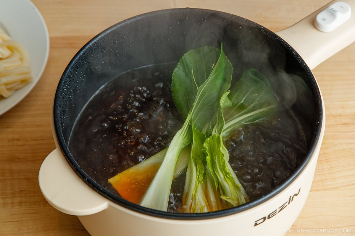 Cooking bok choy in a savory broth in an electric pot.