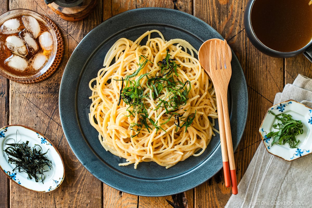 A black round plate containing metaiko pasta - Japanese spaghetti with spicy salted cod roe topped with julienned shiso and shredded nori seaweed.