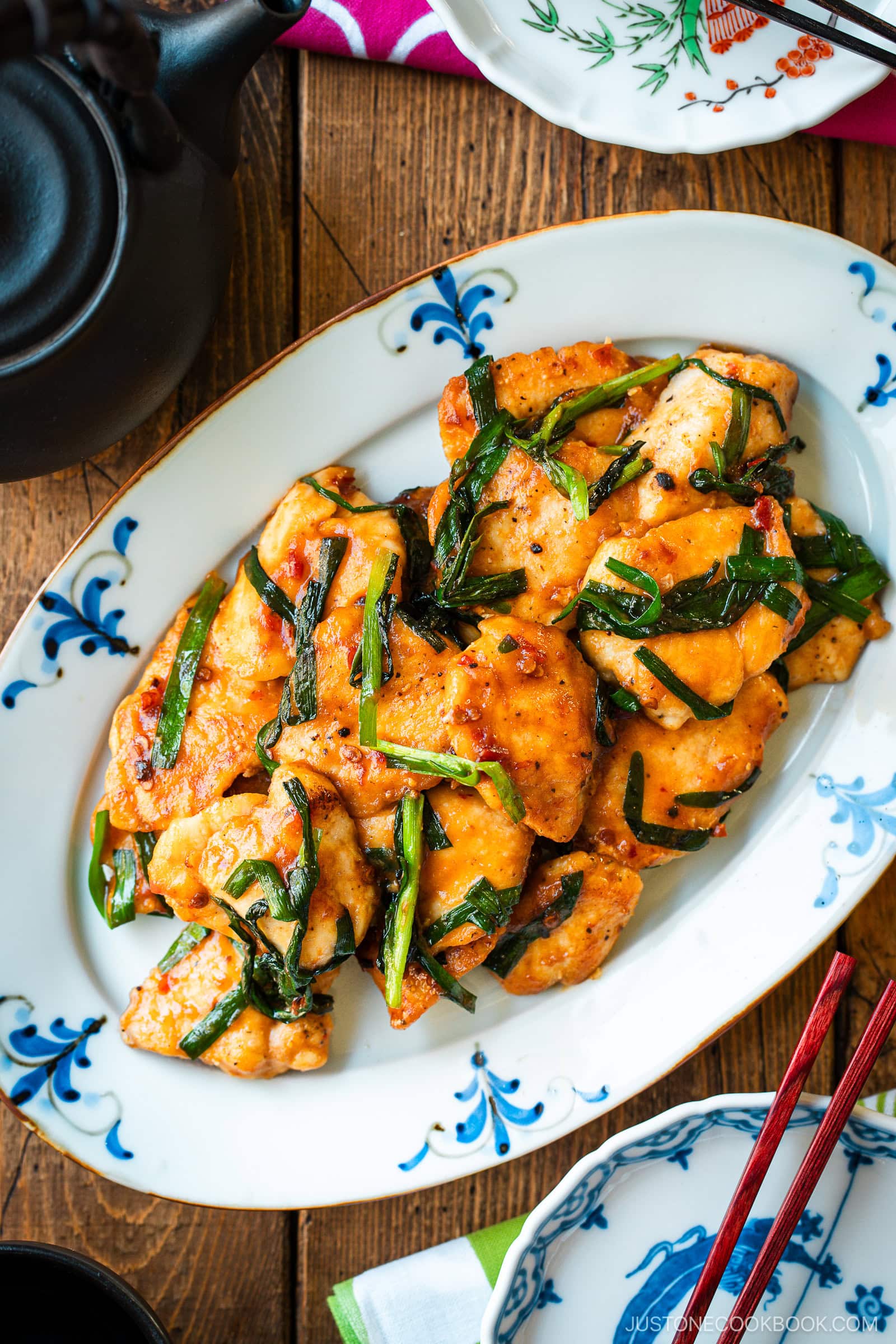 An oval plate containing Chicken Stir-fry with Garlic Chives served on the table along with tea pot and small plates.