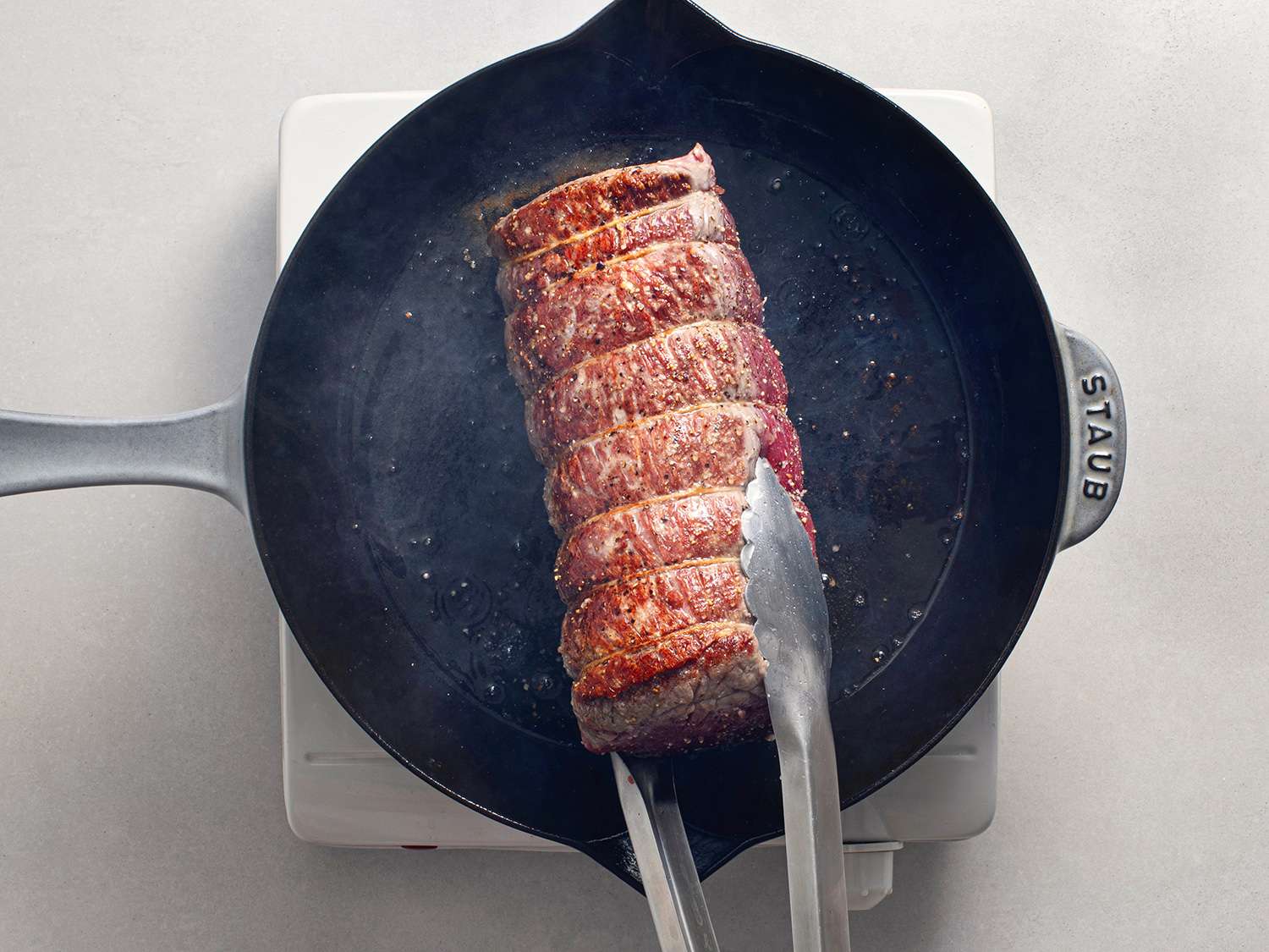 Beef tenderloin being browned in a cast iron skillet.