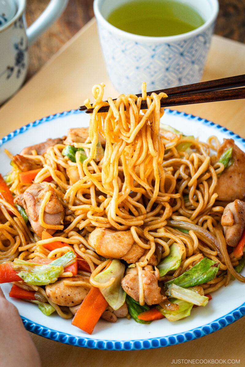 Delicious Chicken Yakisoba with tender, moist chicken thighs and crisp veggies in a sweet savory sauce plated on a beautiful white plate with blue scalloped edge.