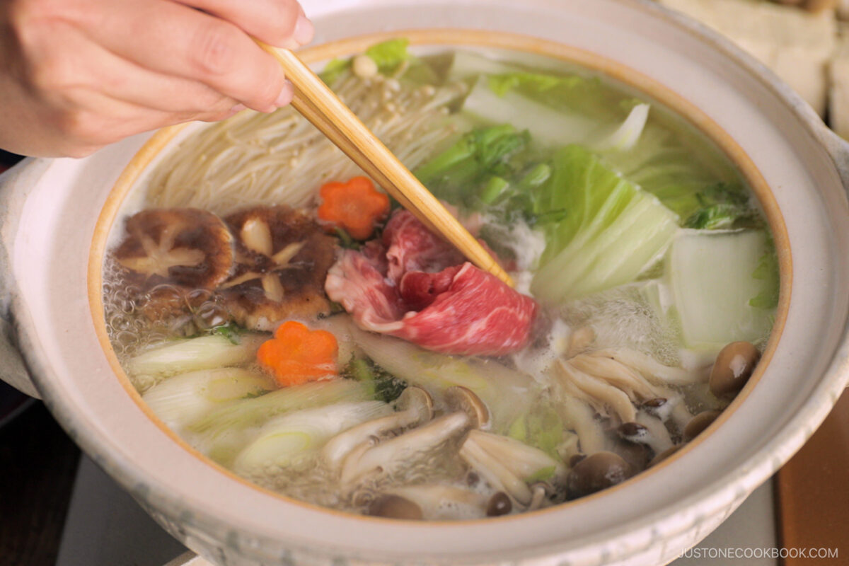Thinly sliced beef is being cooked in the hot pot along with vegetables and tofu in a donabe, Japnaese hot pot.