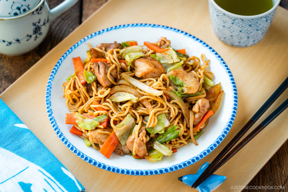 Delicious Chicken Yakisoba with tender, moist chicken thighs and crisp veggies in a sweet savory sauce plated on a beautiful white plate with blue scalloped edge.