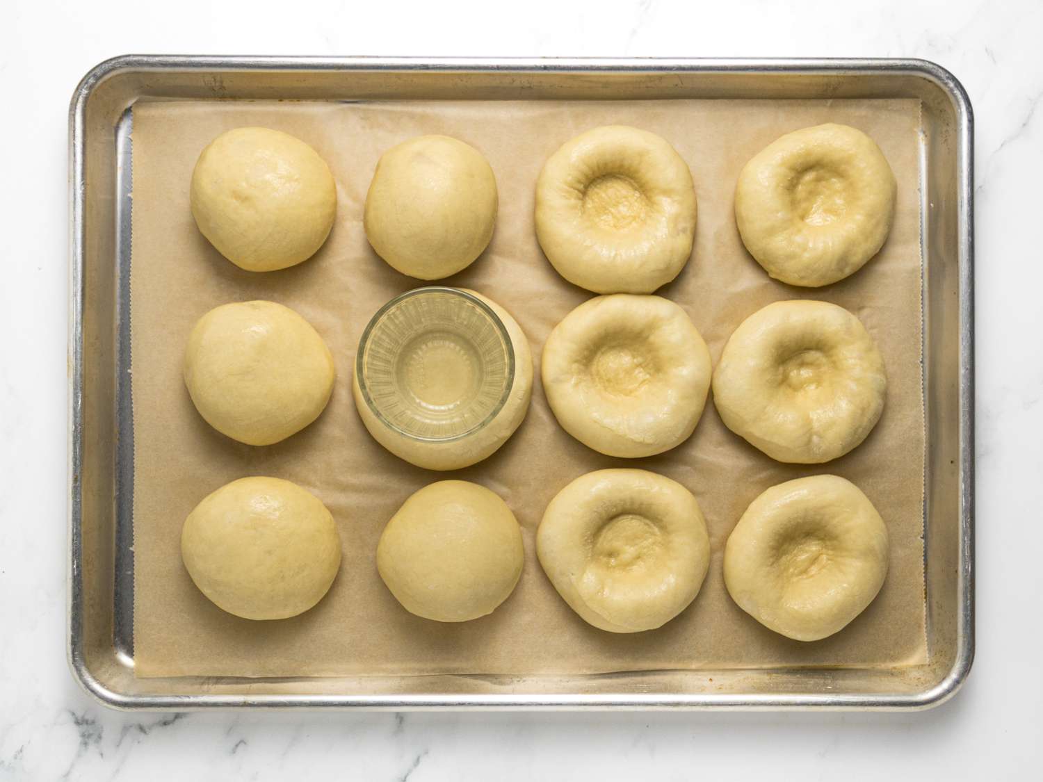 using the bottom of a glass to shape a dent into thee Kolches on a sheetpan 