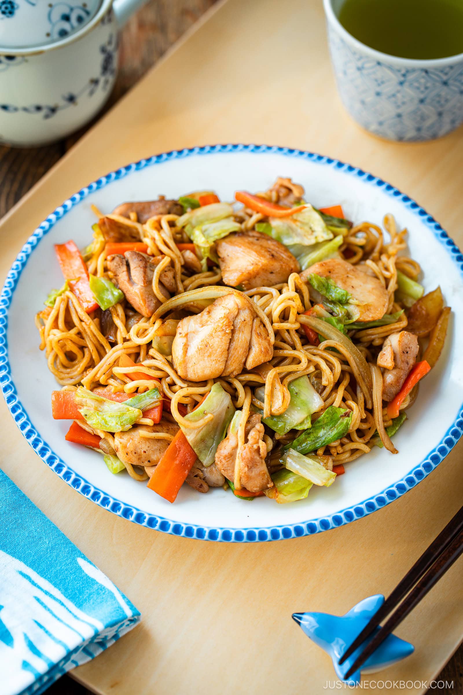 Delicious Chicken Yakisoba with tender, moist chicken thighs and crisp veggies in a sweet savory sauce plated on a beautiful white plate with blue scalloped edge.