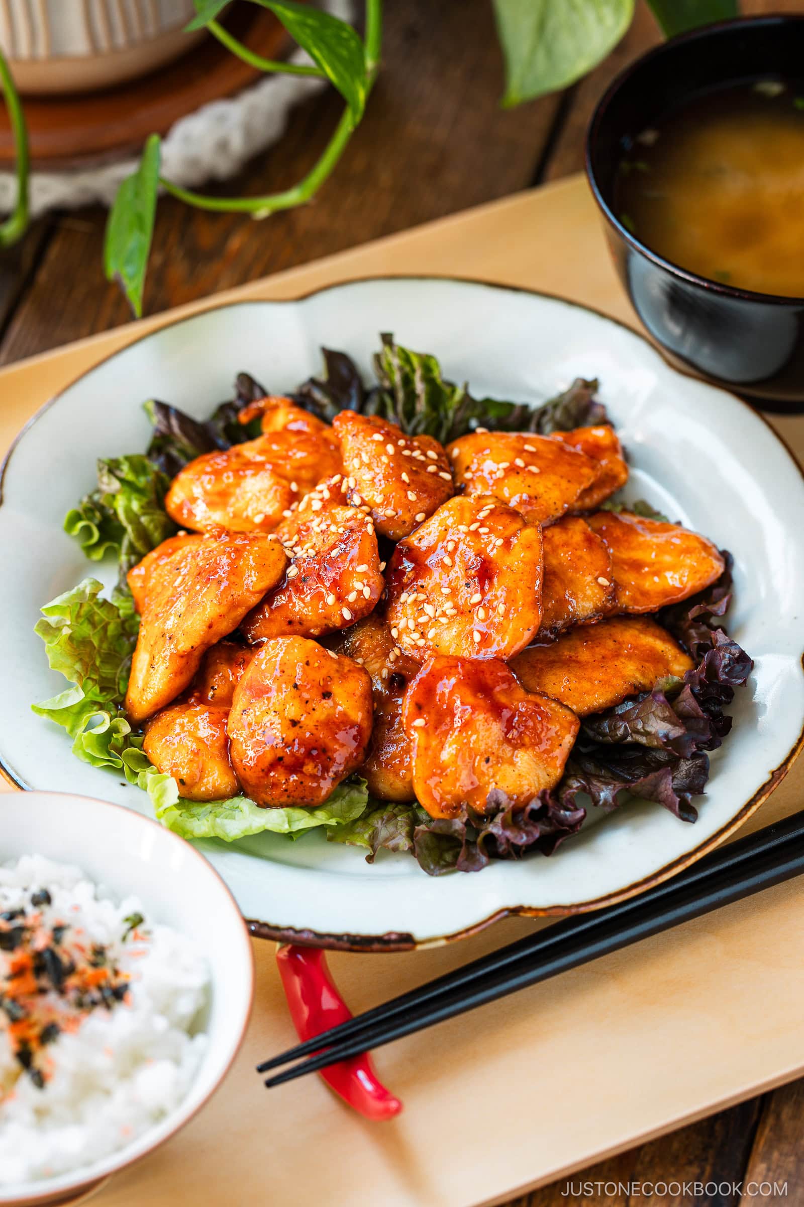 A white plate containing Honey Gochujang Chicken sprinkled with sesame chicken served on green salad.