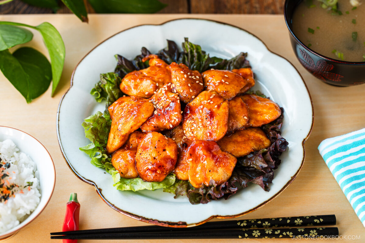 A white plate containing Honey Gochujang Chicken sprinkled with sesame chicken served on green salad.