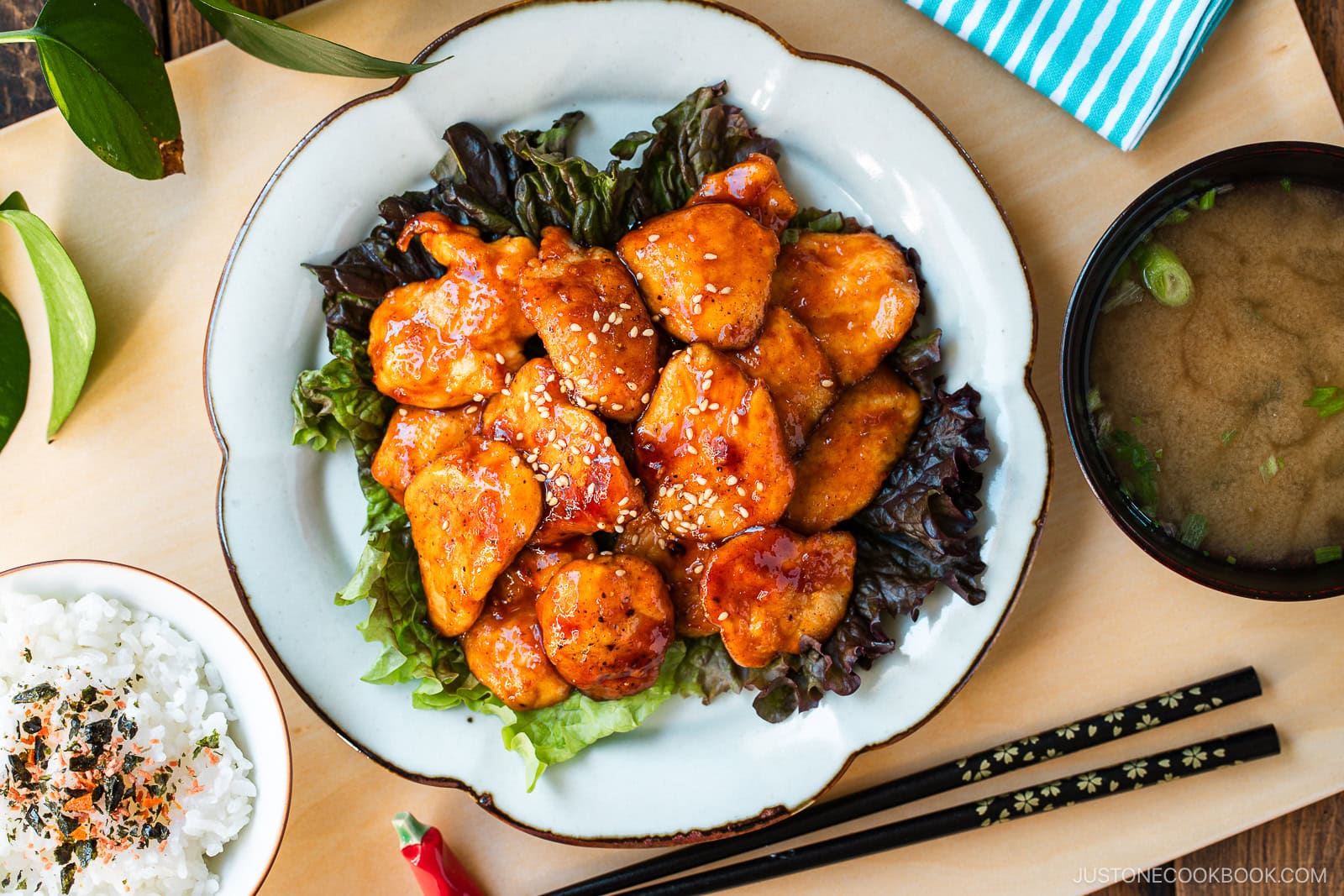 A white plate containing Honey Gochujang Chicken sprinkled with sesame chicken served on green salad.