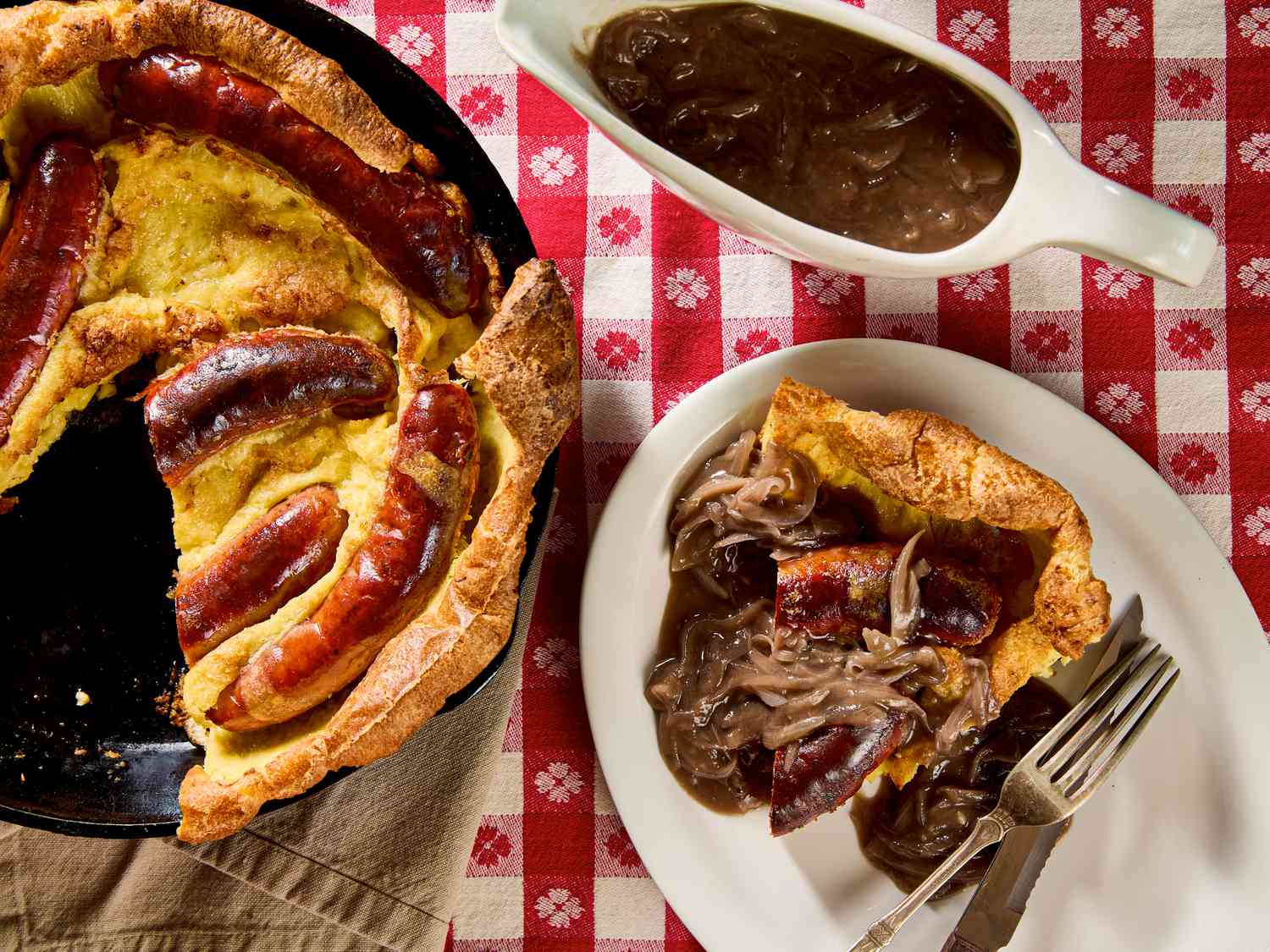 A pan with toad in the hole and a plate with a serving and onion gravy on a checkered tablecloth