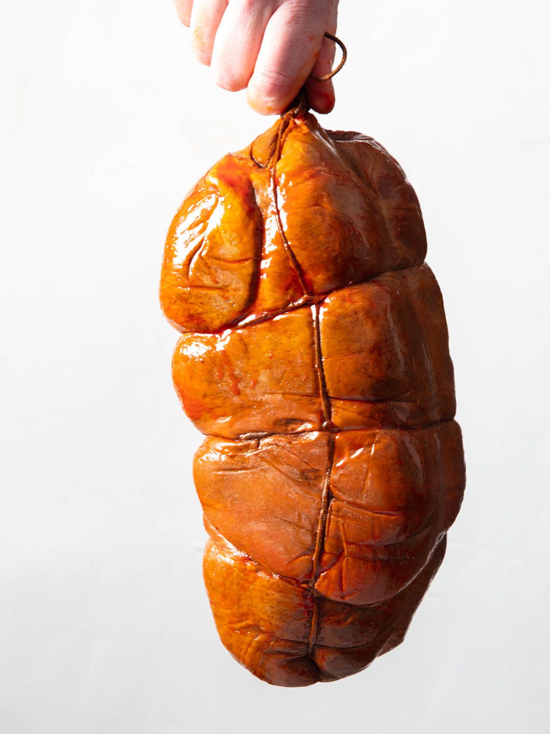 An uncut 'nduja is held by a hand from a string. 