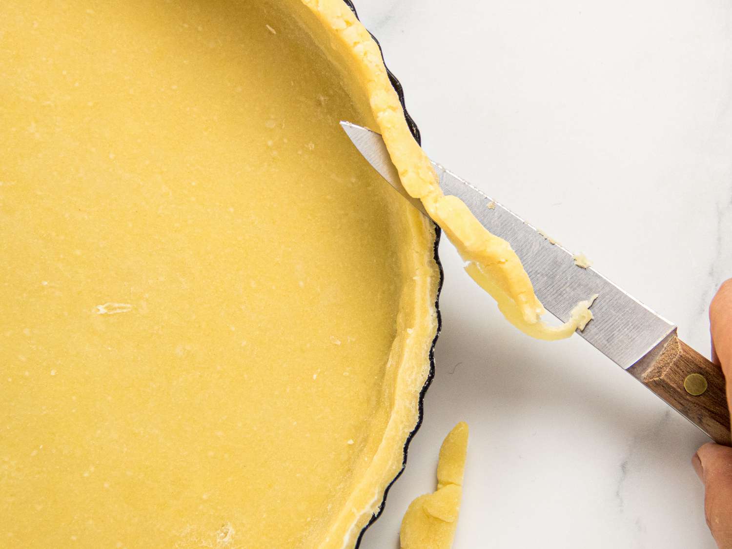 A close-up of a tart crust being trimmed with a knife in preparation for baking