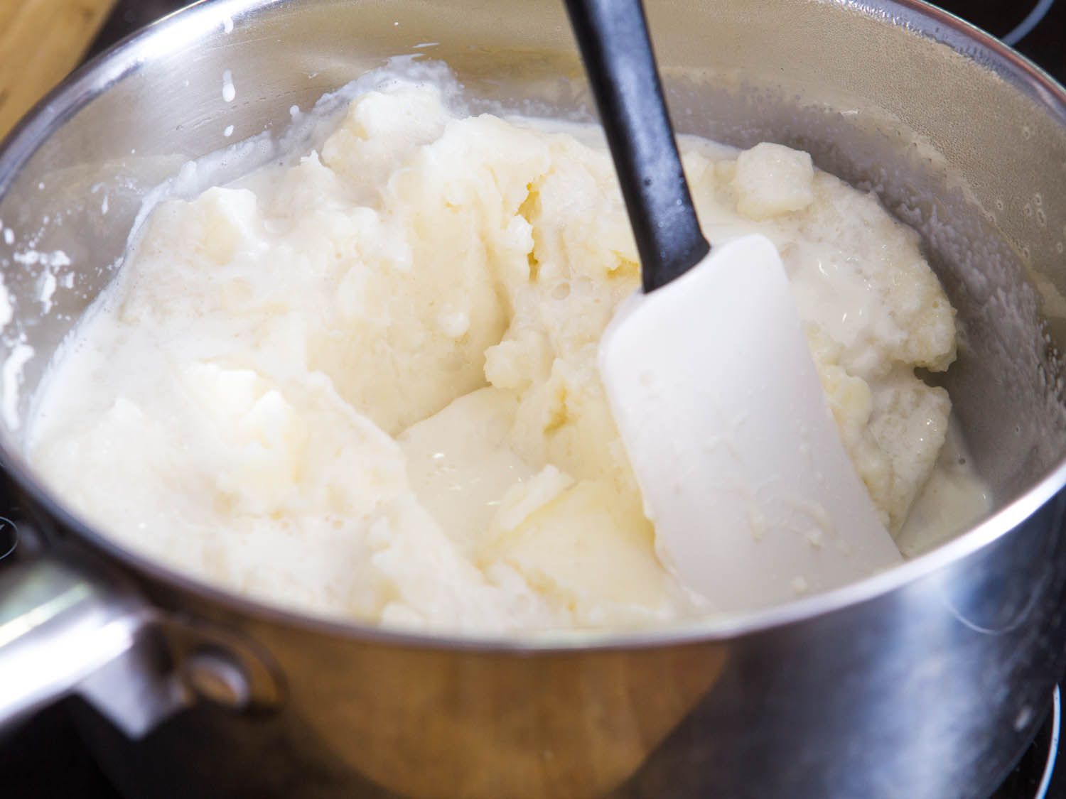 Spatula mixing mashed potatoes with cream in a pot.