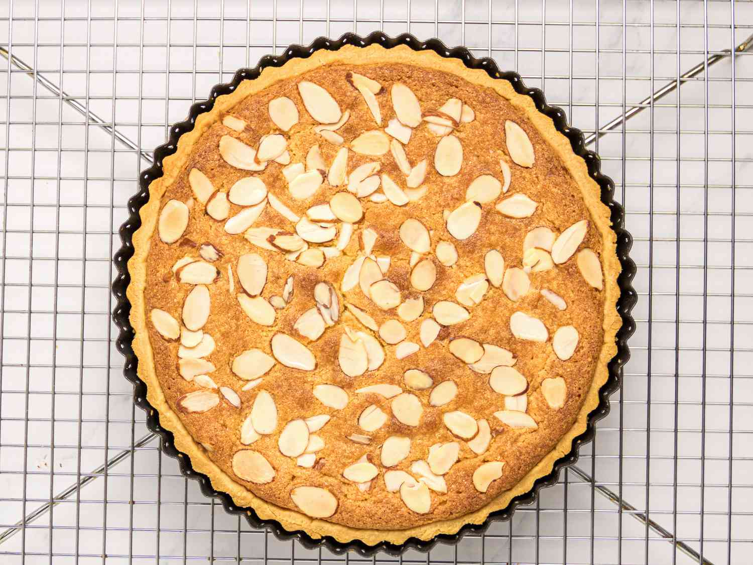 A bakewell tart with almond slices on top, placed on a cooling rack