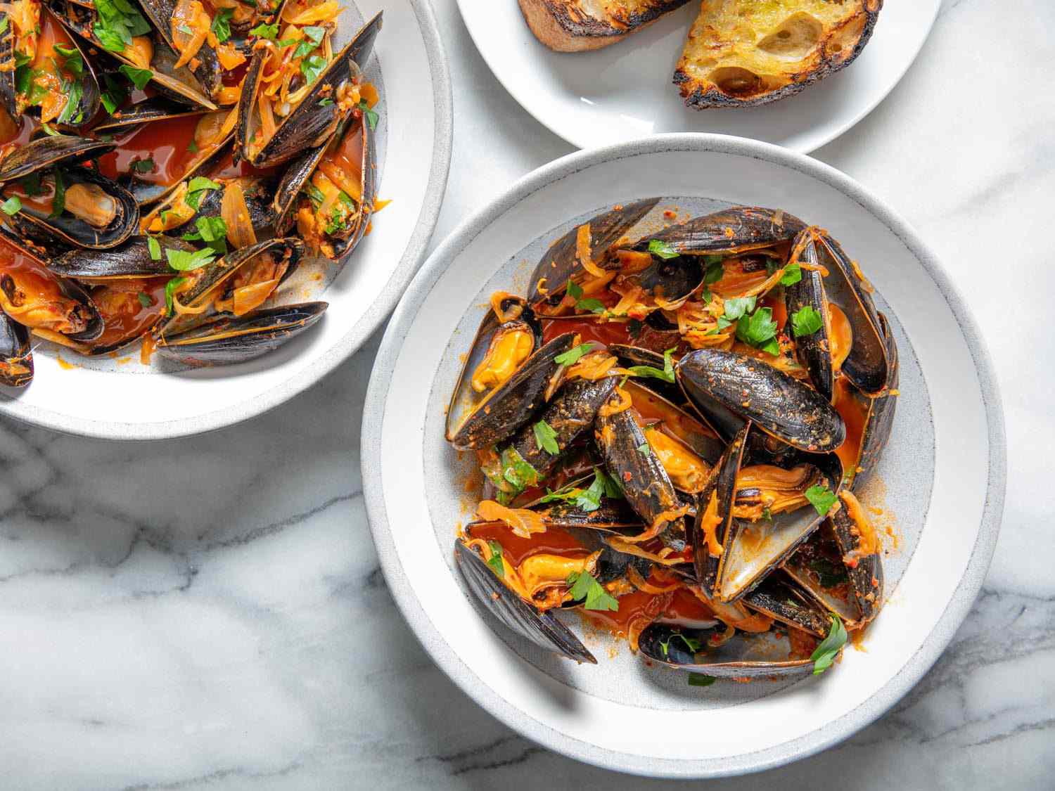 Overhead of two serving bowls with steamed mussels and 'nduja and a side of charred bread.