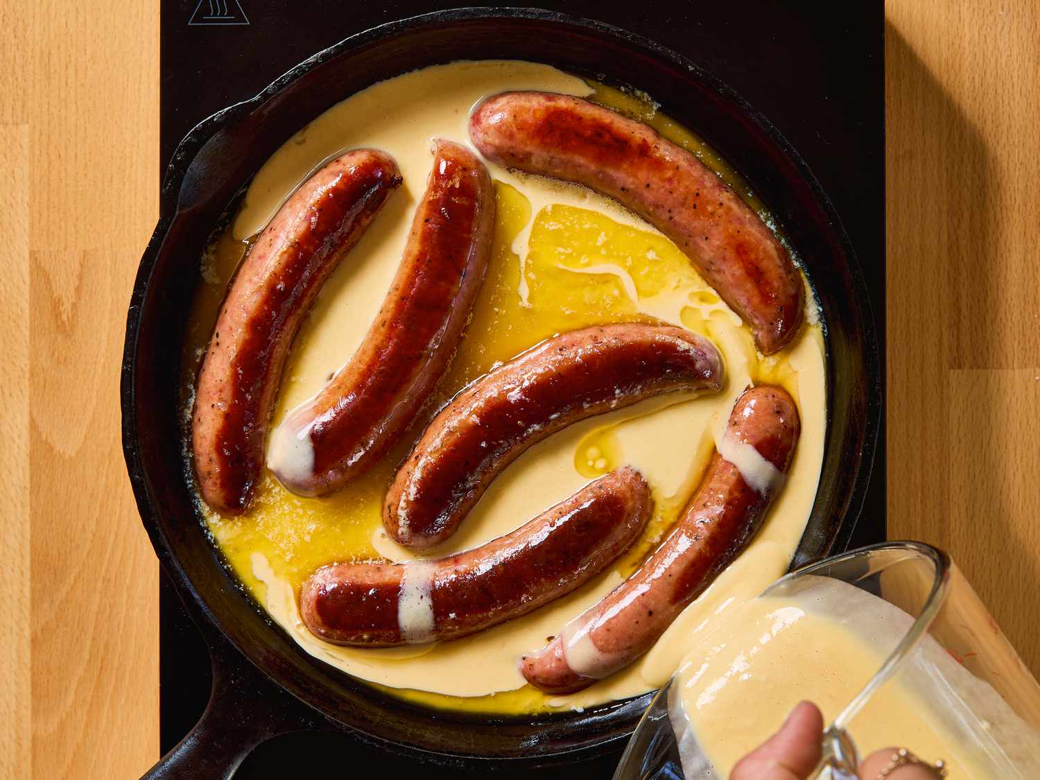 Sausages in a skillet with batter being poured in