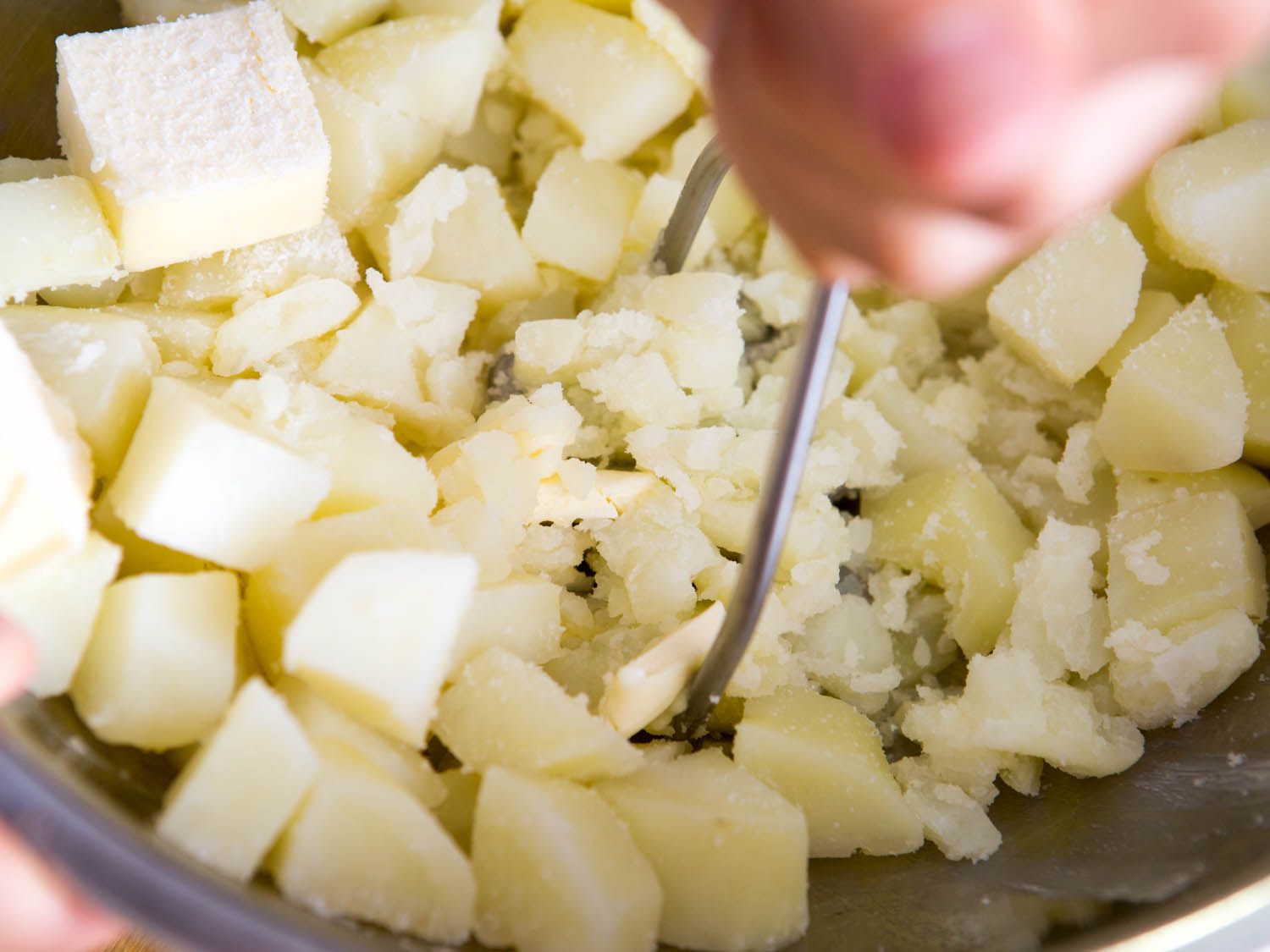 Closeup of boiled potatoes being mashed by hand with a potato masher.