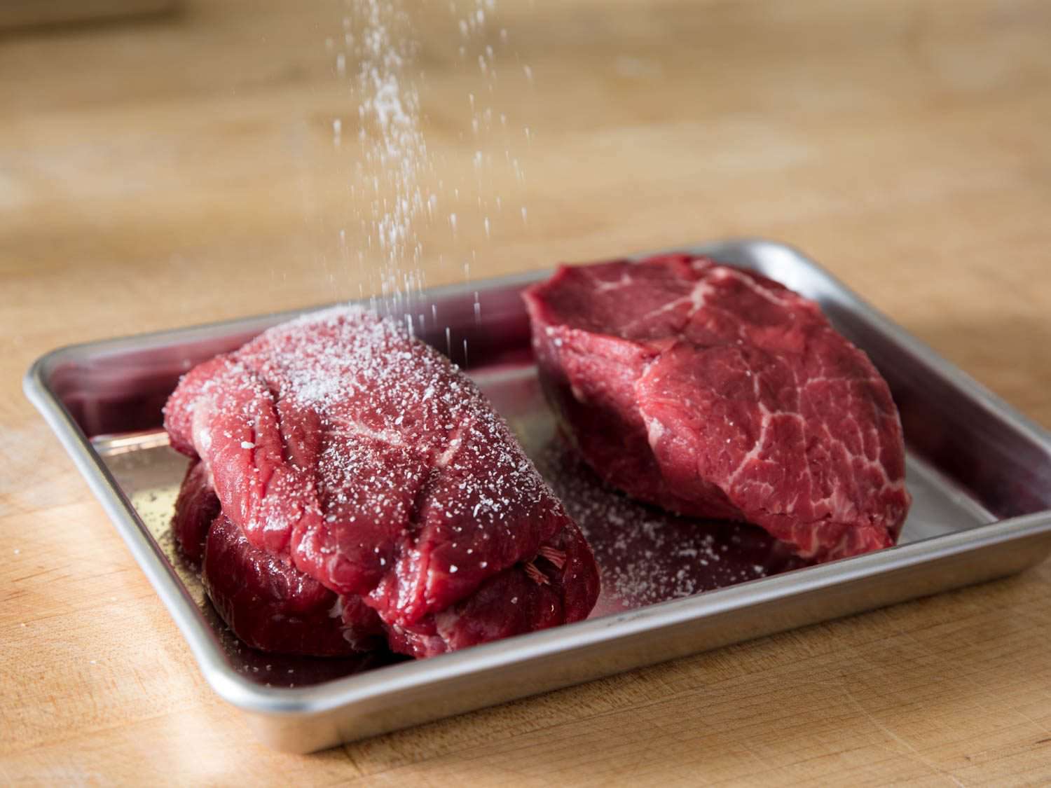 Steaks being showered with salt.