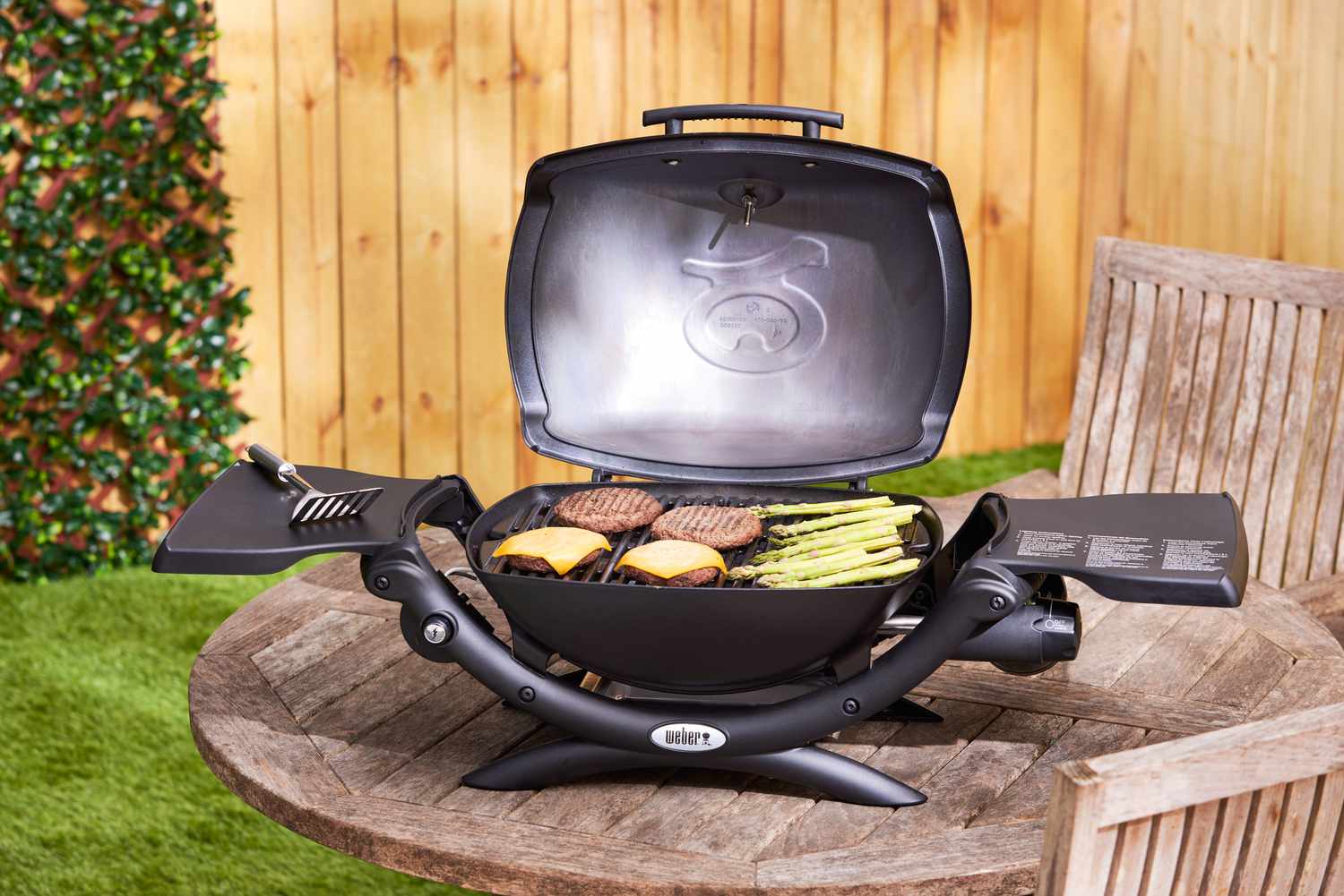 A Weber portable grill cooking burgers and asparagus. 