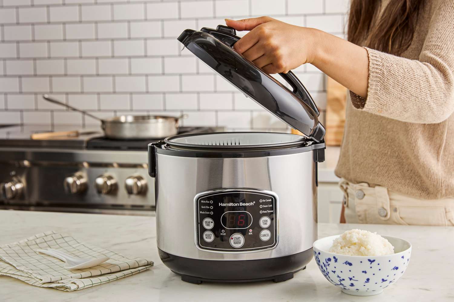  A person lifting the lid of the Hamilton Beach rice cooker.