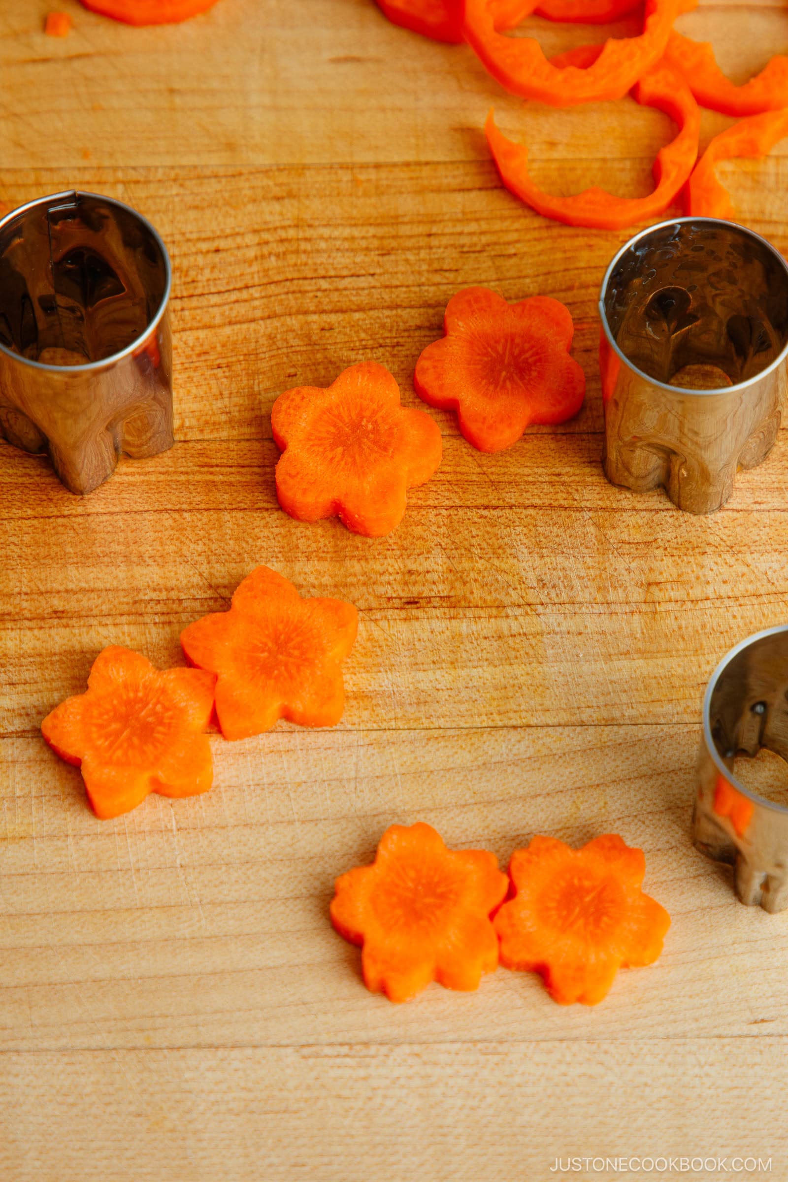 Sliced carrots cut into flower shapes on a wooden cutting board, with metal flower-shaped vegetable cutters nearby.