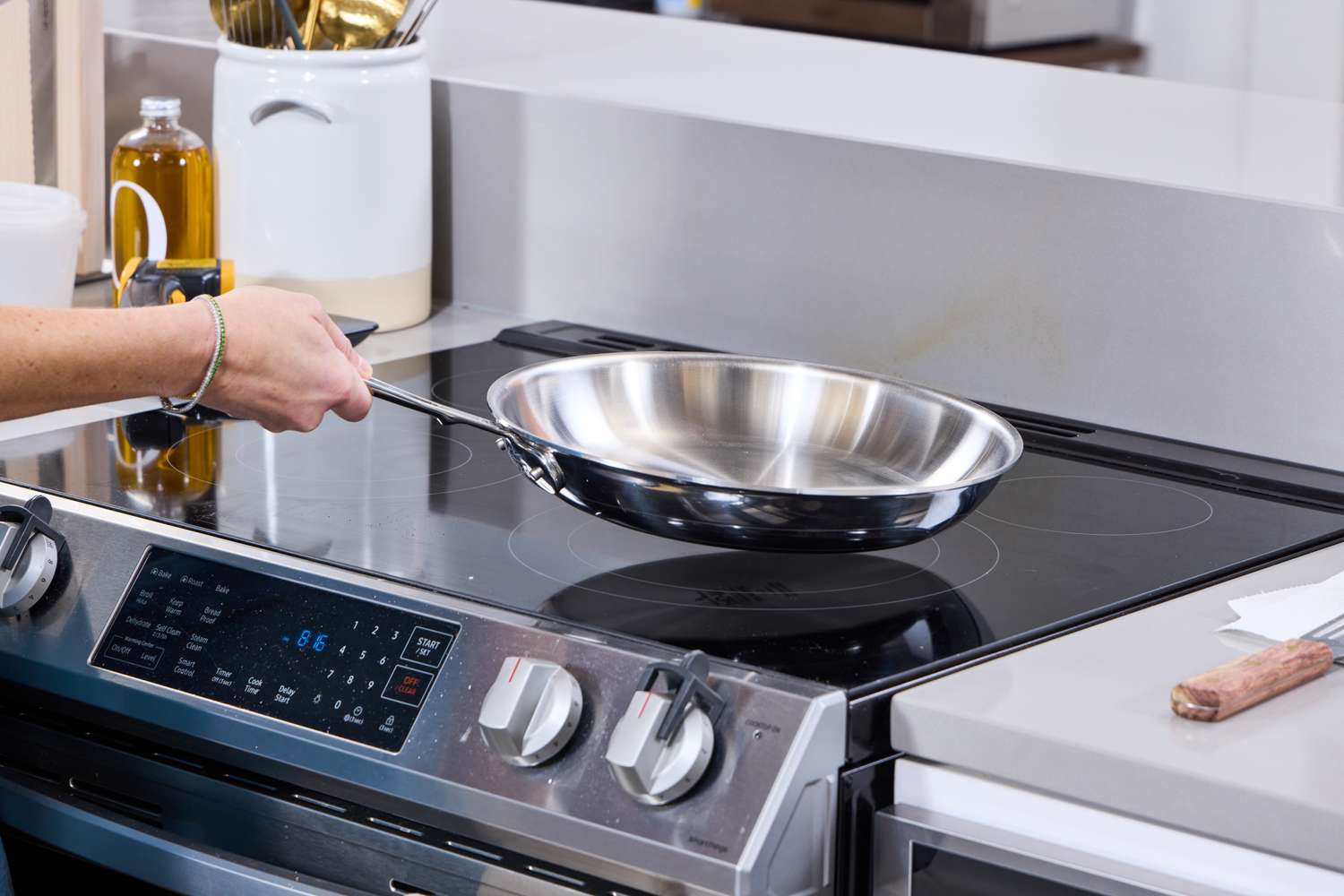 A hand holding a frying pan over a modern stovetop in a kitchen