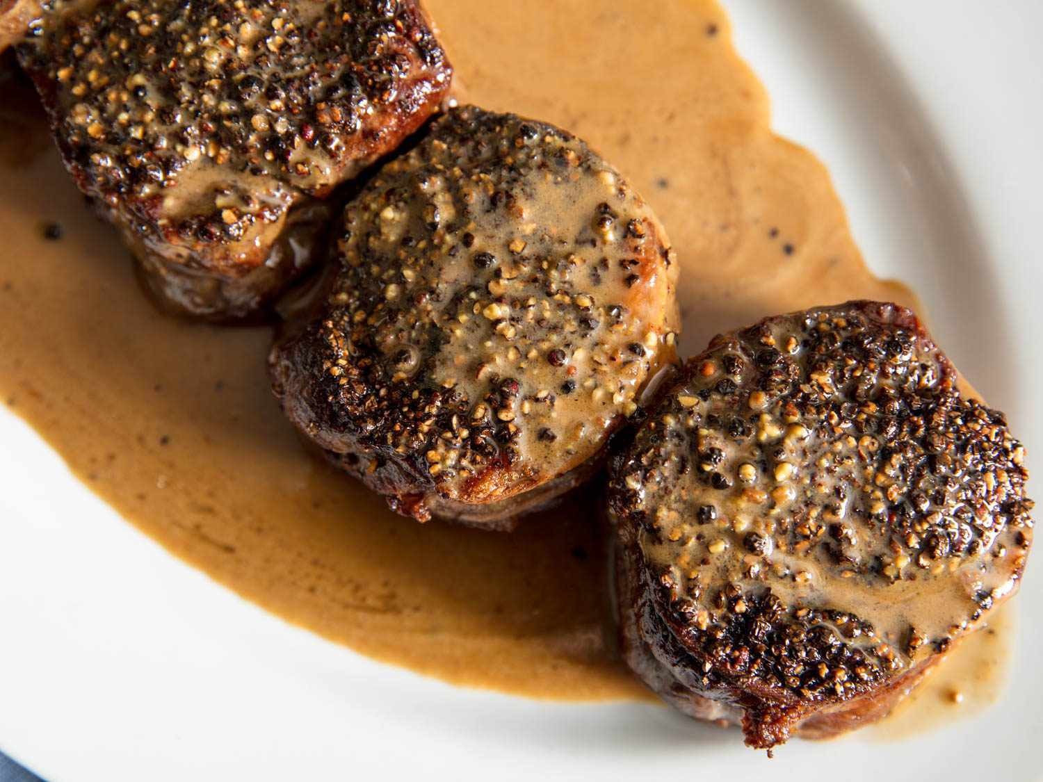 Overhead shot of several steaks au poivre on a porcelain platter, smothered with a creamy pan sauce.