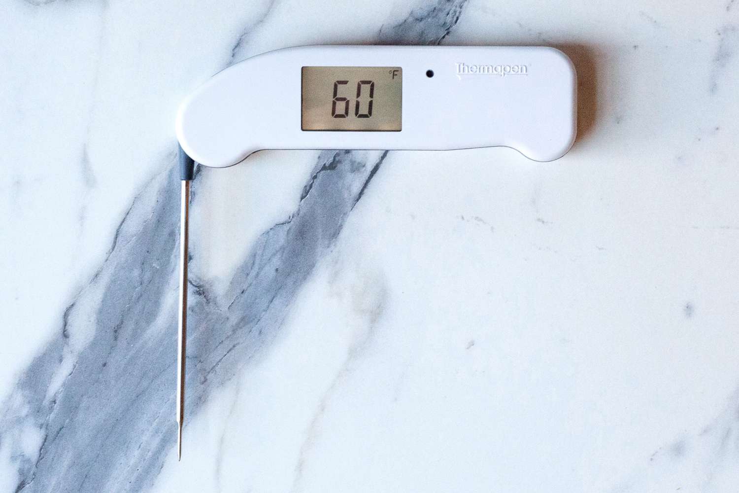 A white Thermapen ONE thermometer with its probe extended on a marble countertop.