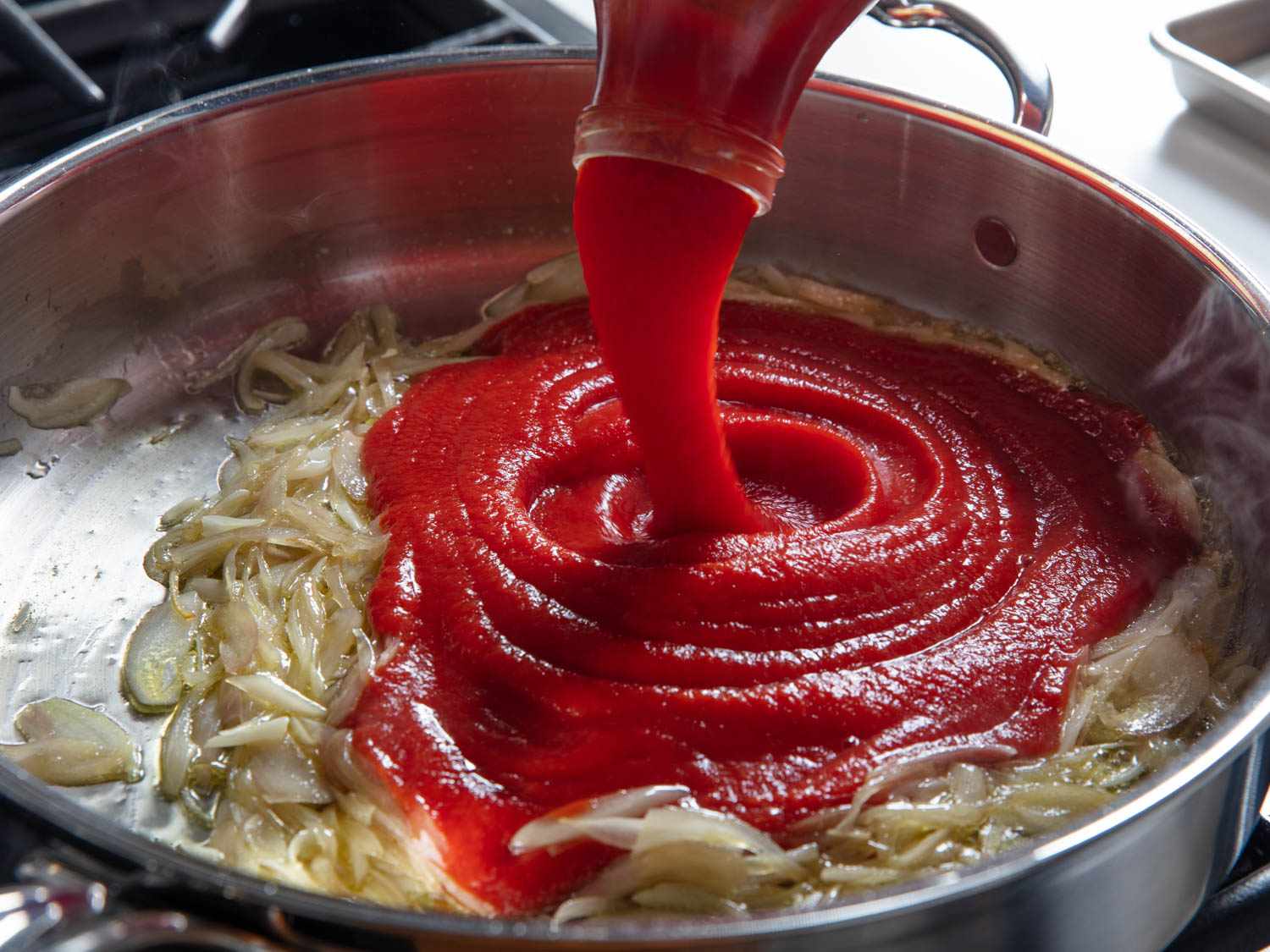 Passata being poured into a pan with browned onions.