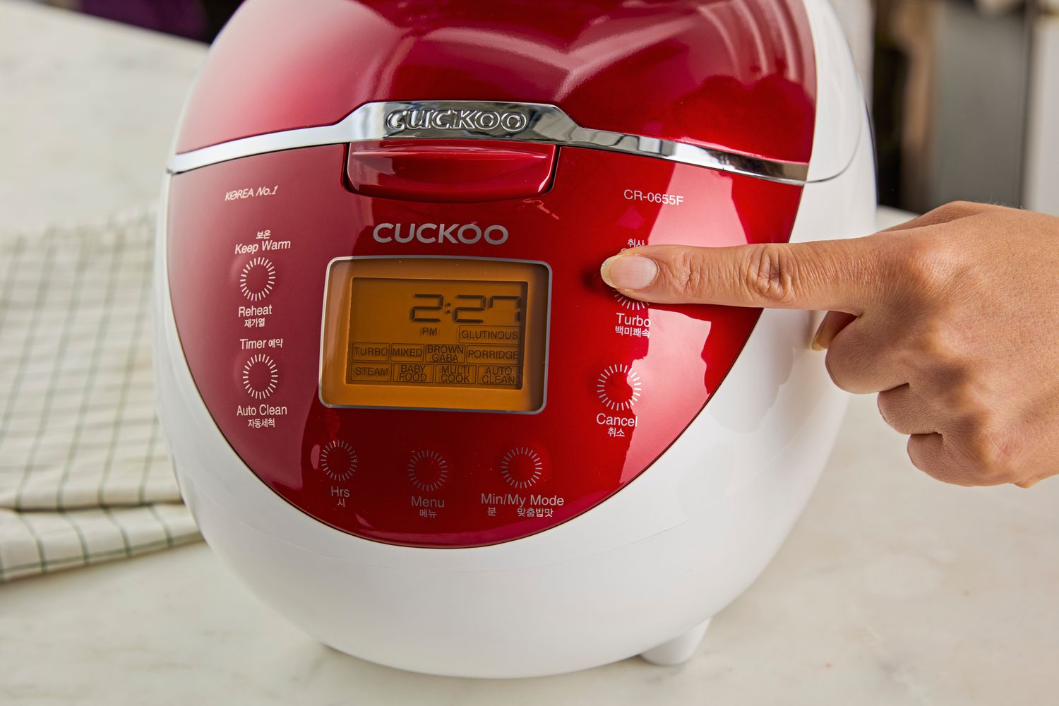 A person pressing the control panel of the Cuckoo rice cooker.